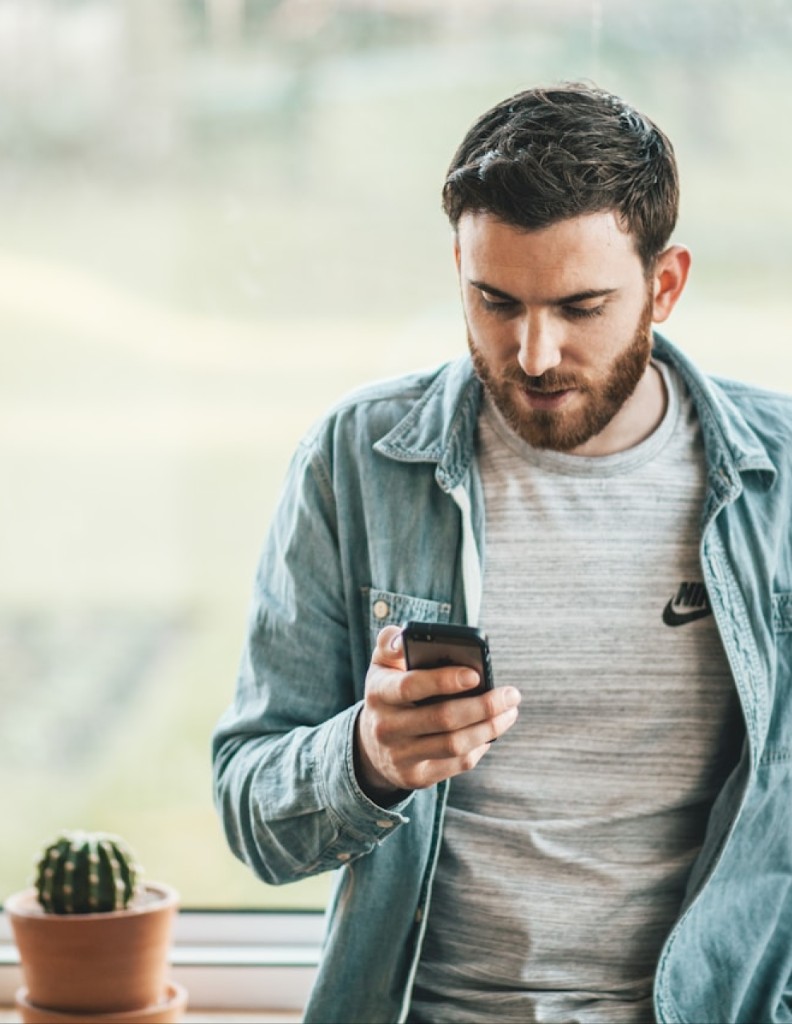 Mann mit Smartphone neben Fenster und Kaktus
